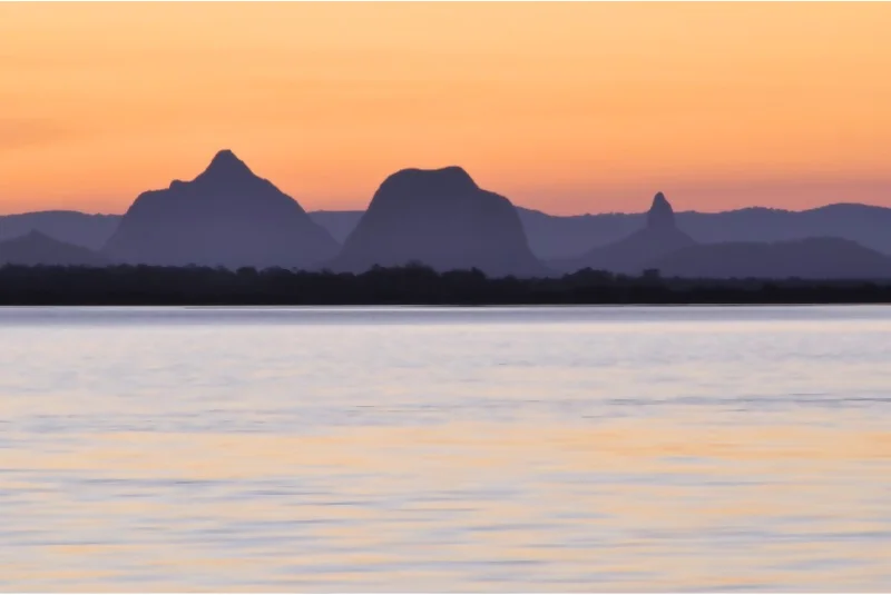 Looking over water to Glasshouse mountains in front of a sunset